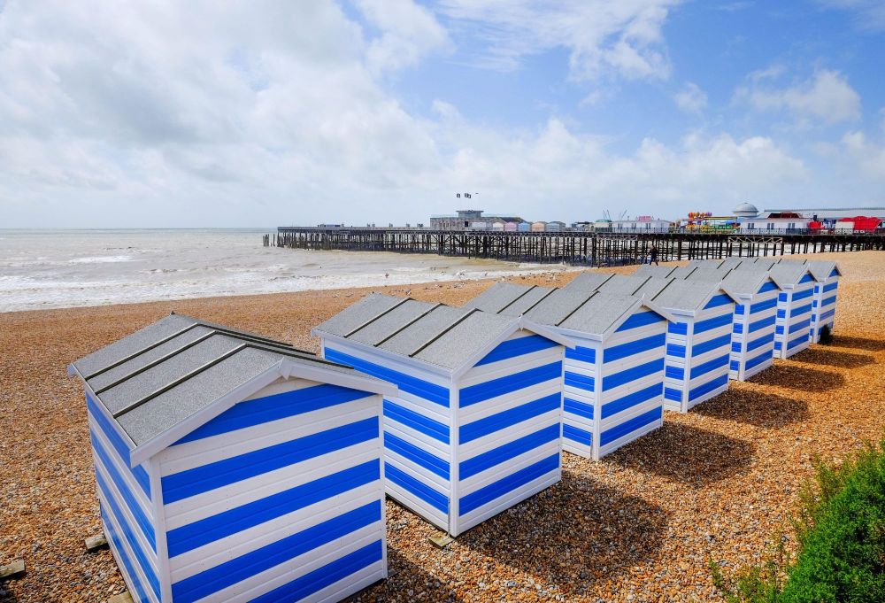 Blue and white striped beach huts on the pebble beach at St Leonards-on-Sea, with Hastings Pier in the background