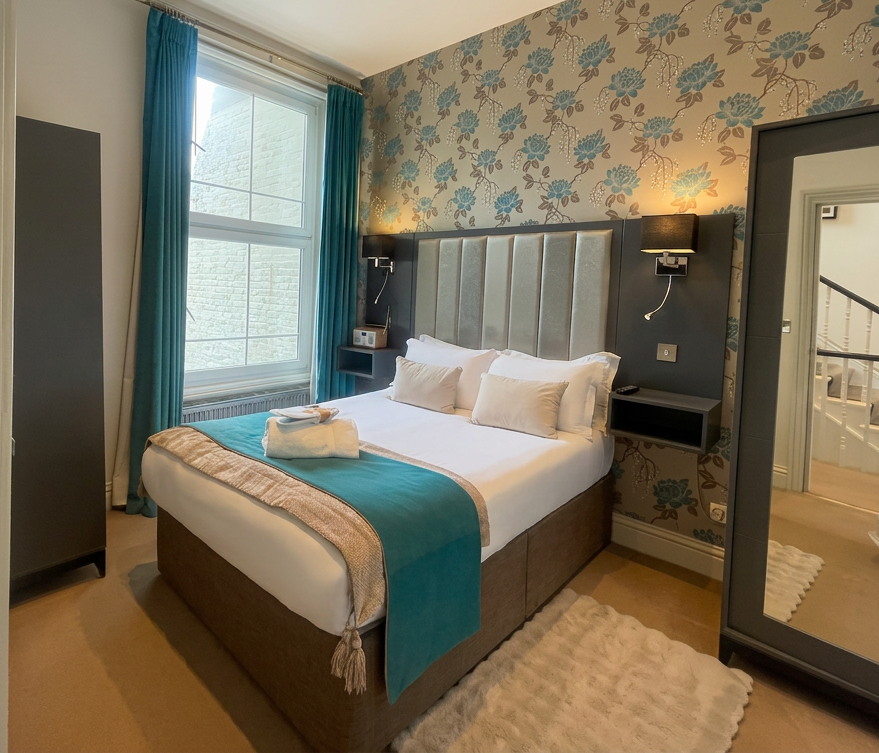 Hastings House bedroom with teal floral wallpaper and silver channel headboard